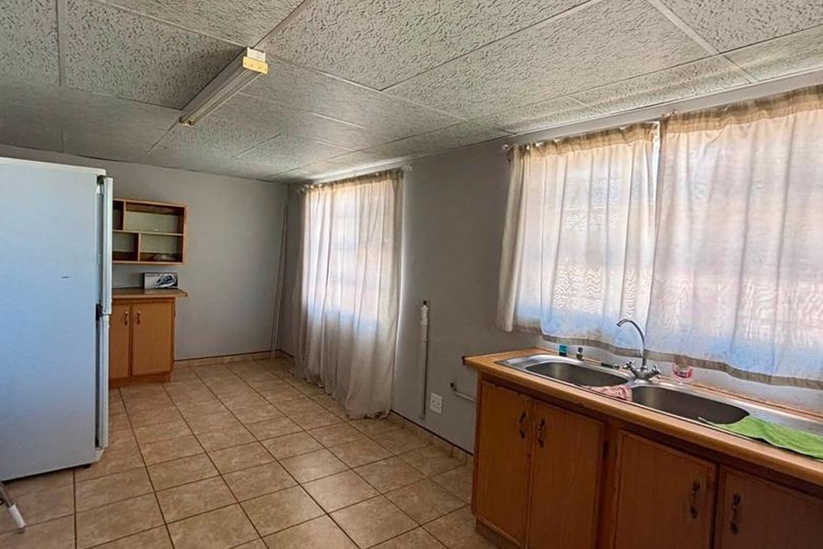 A functional kitchen featuring tiled flooring, fitted wooden cabinetry, and a double bowl sink, offering potential for modernization and aesthetic updates.