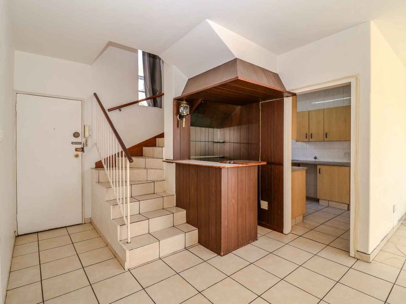 Open plan living area featuring a built-in bar, tiled staircase with wooden handrail, and direct access to a functional kitchen space.