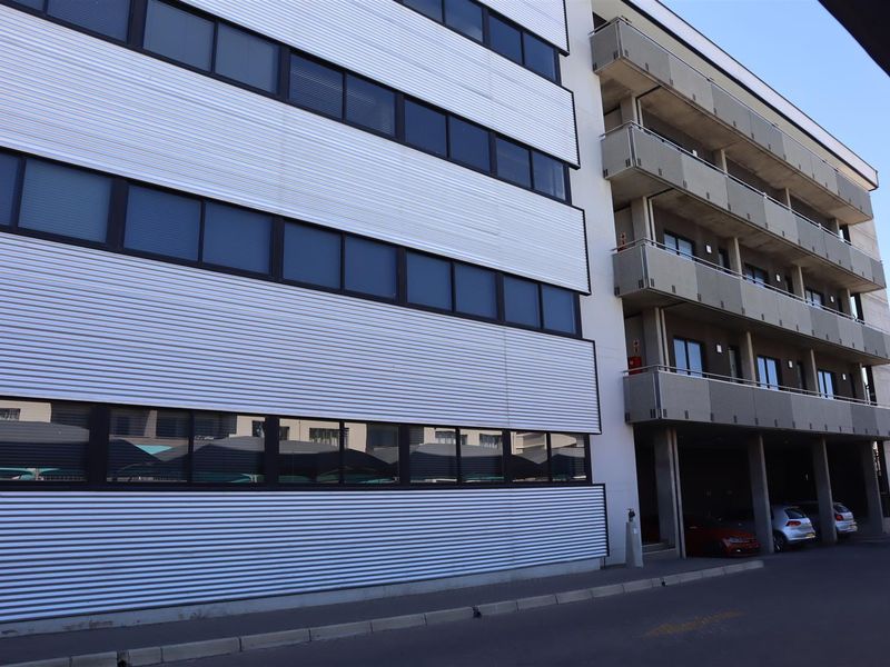 A multi-story office building exterior featuring corrugated metal cladding, rows of aluminum-framed windows, and integrated balconies.