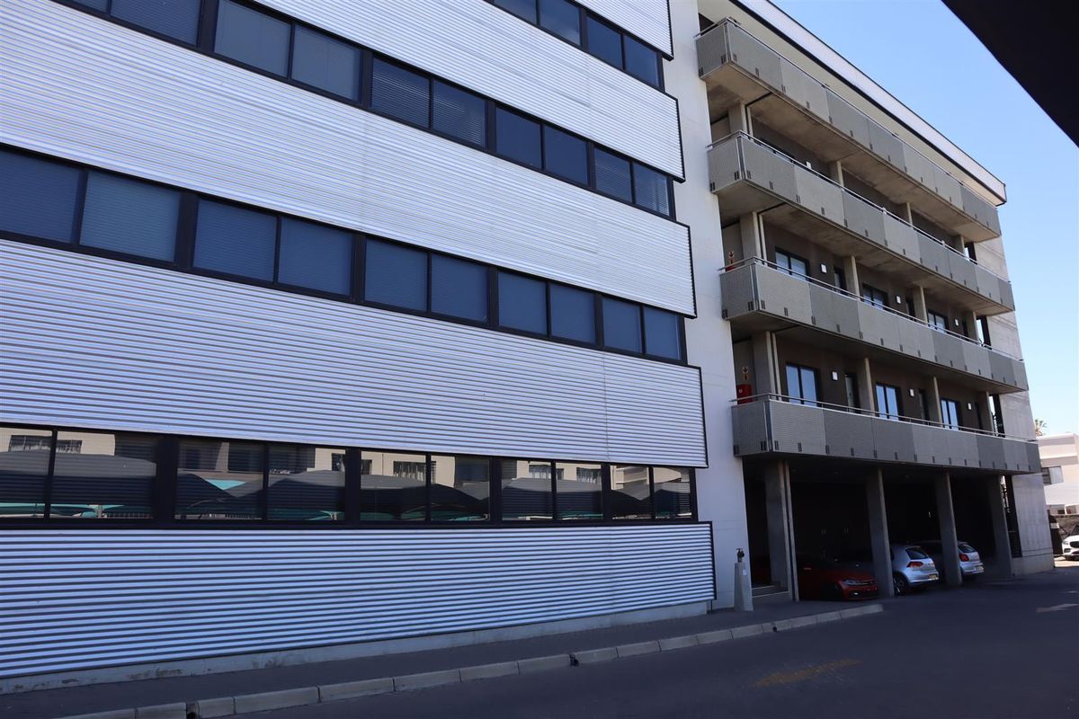 A multi-story office building exterior featuring corrugated metal cladding, rows of aluminum-framed windows, and integrated balconies.