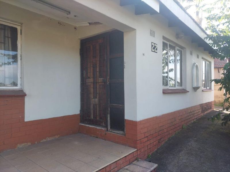 Front entrance of a single-story house featuring a tiled porch, brick base, and security gate, showing signs of exterior wear and maintenance requirements.