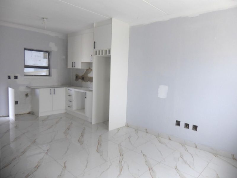 An open-plan kitchen area featuring white cabinetry and marble-look floor tiles, currently in an unfinished state requiring final wall finishes and electrical completion.