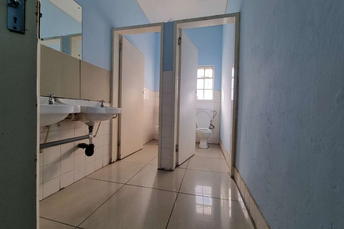 A functional communal bathroom facility featuring dual wall-mounted basins, tiled flooring, and two separate toilet cubicles with privacy doors.