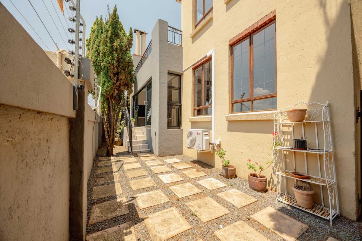 A side exterior view of the property featuring a paved walkway, gravel landscaping, boundary wall with electric fencing, and an external air conditioning unit.
