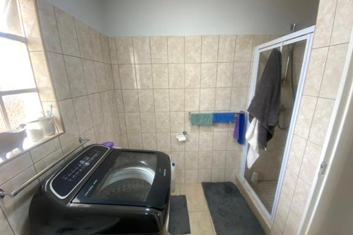 A functional bathroom featuring a glass-enclosed shower, tiled walls, and dedicated space for a top-loading washing machine.