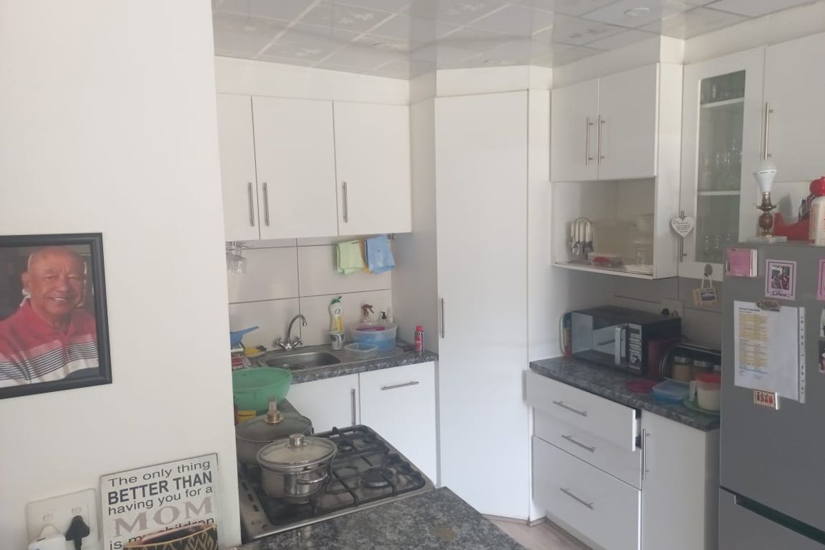 A compact kitchen featuring white cabinetry, granite-look countertops, a built-in gas hob, and a stainless steel sink.