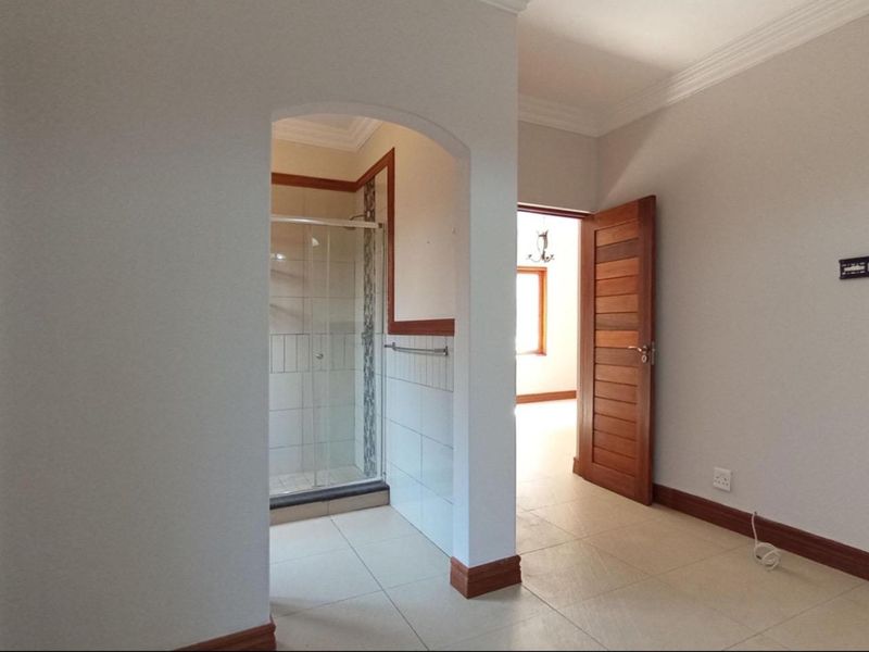 An empty bathroom featuring a glass shower enclosure, tiled flooring, and a wooden door, leading into an adjacent room.