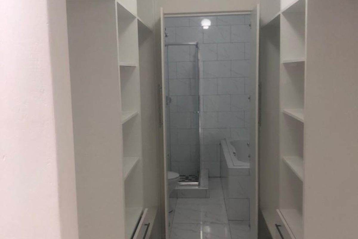 A walk-through dressing area with built-in cabinetry leading directly into a modern bathroom featuring a shower and bathtub.