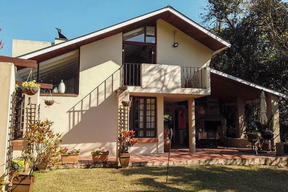 Rear elevation of a double-story house featuring a covered patio with a built-in braai, a balcony, and terracotta tiled flooring overlooking the garden.