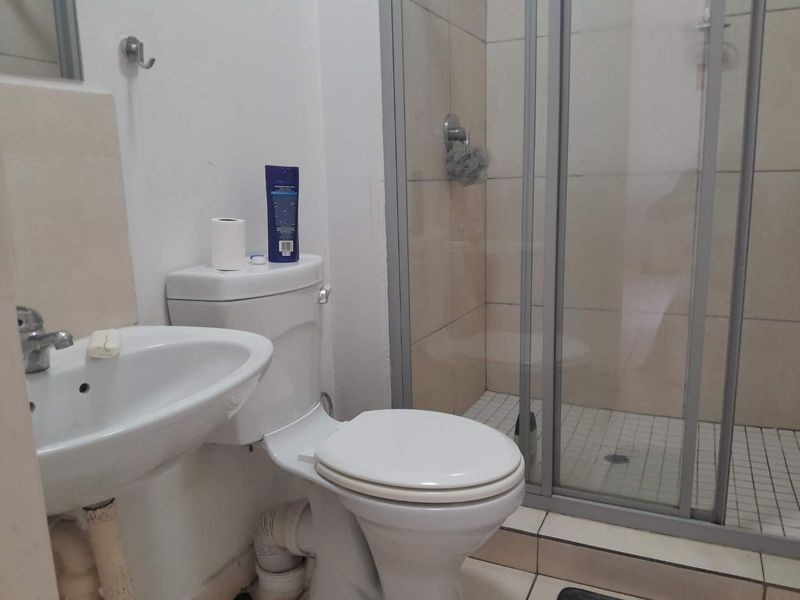 A functional bathroom featuring a pedestal basin, toilet, and a glass-enclosed shower with tiled finishes.