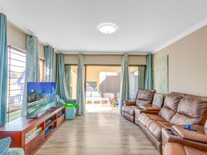 A well-lit living room featuring laminate flooring, cove cornicing, and large sliding glass doors that provide direct access to the outdoor patio area.