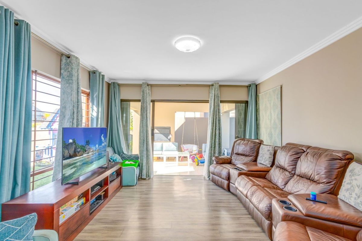 A well-lit living room featuring laminate flooring, cove cornicing, and large sliding glass doors that provide direct access to the outdoor patio area.