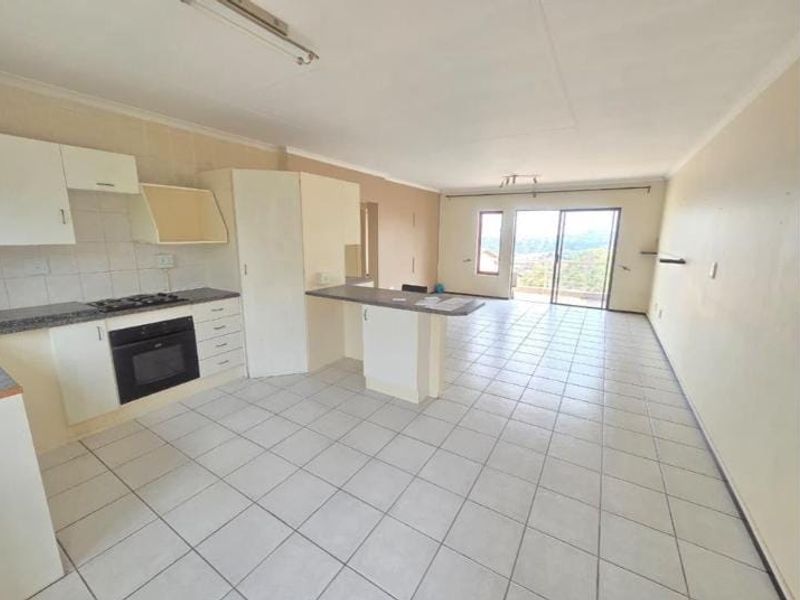 Spacious open-plan kitchen and living area featuring tiled floors, built-in cabinetry, and sliding doors leading to an outdoor balcony with scenic views.