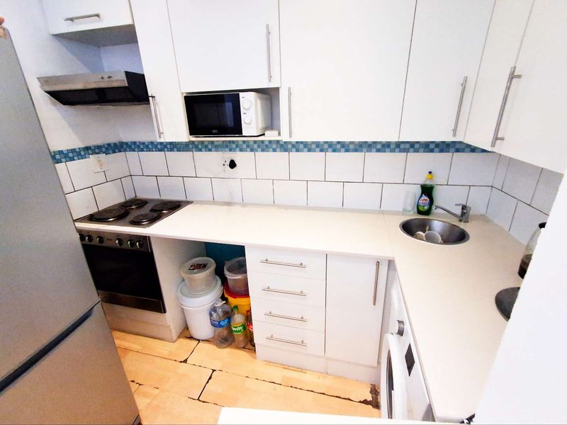 Compact kitchen featuring white cabinetry, built-in oven and hob, tiled backsplash, and integrated sink, with visible wear to the flooring.