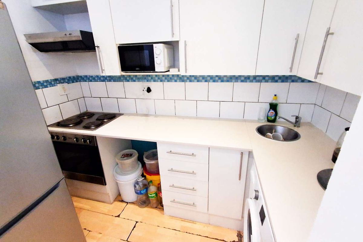 Compact kitchen featuring white cabinetry, built-in oven and hob, tiled backsplash, and integrated sink, with visible wear to the flooring.