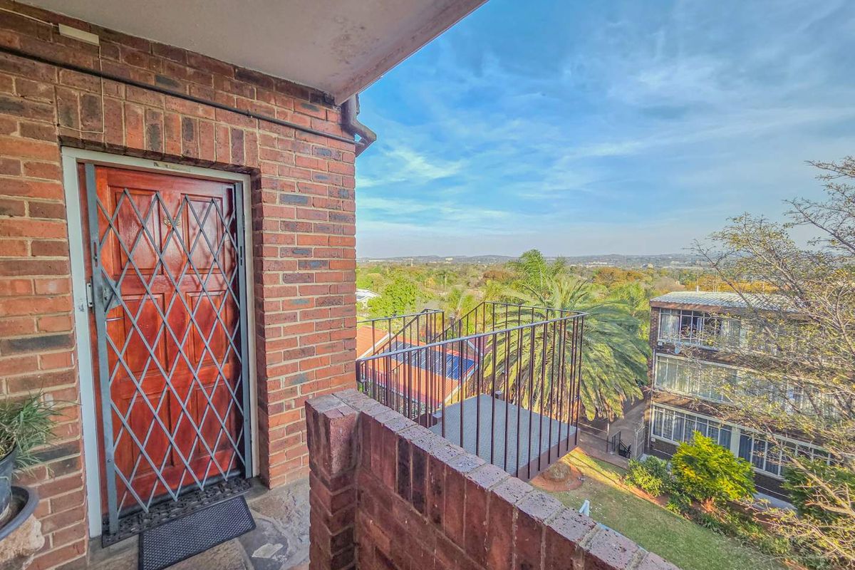 An elevated balcony featuring brick walls, a security gate, and metal railings, offering an open view of the surrounding neighborhood.