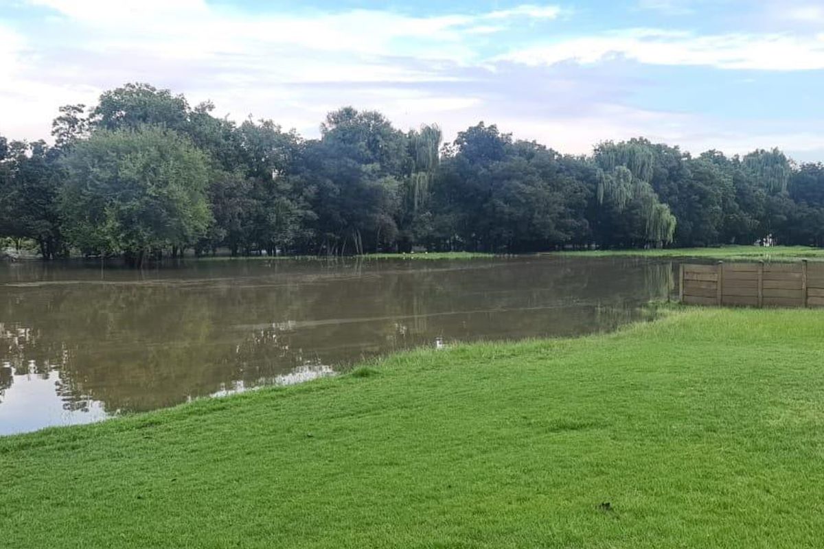 A view of the agricultural land featuring a large body of water, mature trees, and a perimeter fence.