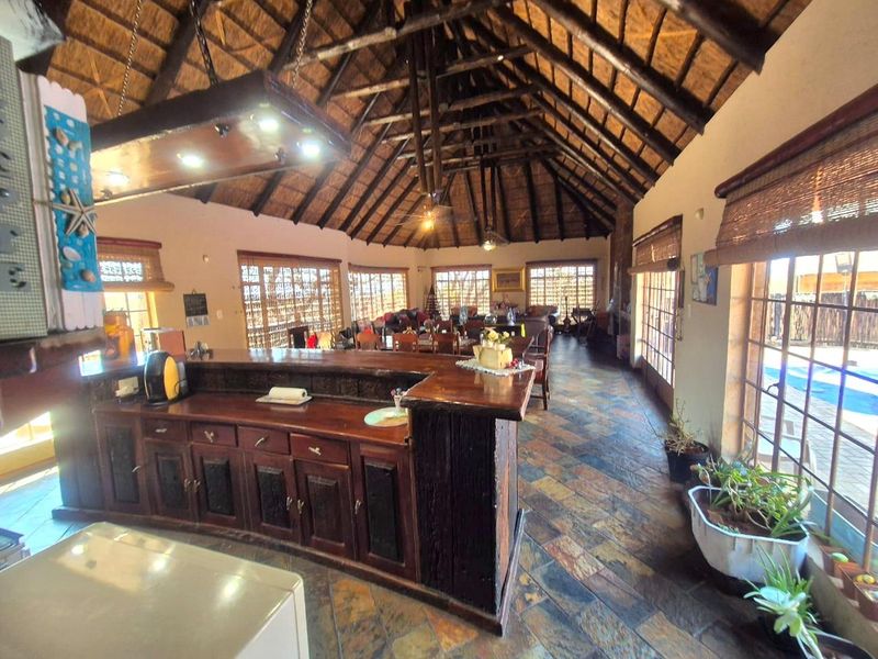 Spacious open-plan living area featuring a high thatched roof with exposed timber trusses, a built-in bar, and slate tile flooring throughout.
