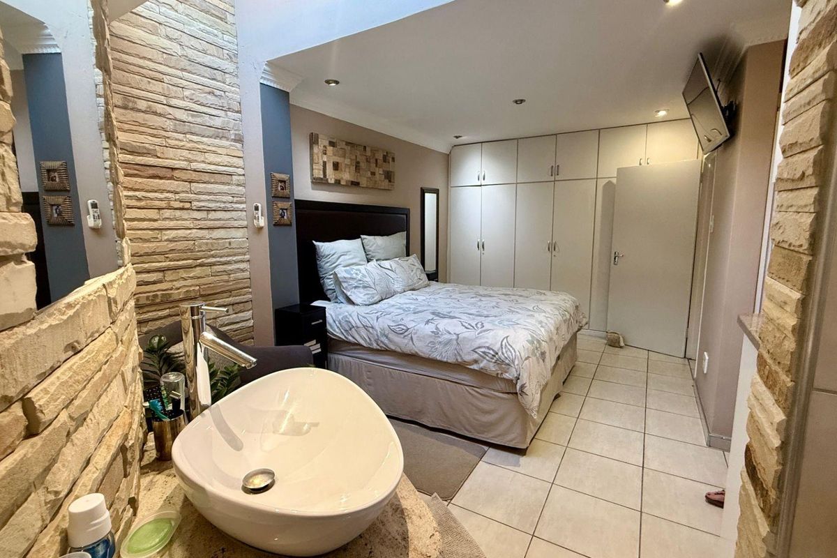 Bedroom featuring built-in cupboards, tiled flooring, and an integrated vanity area with a modern vessel sink and stone-cladding feature wall.