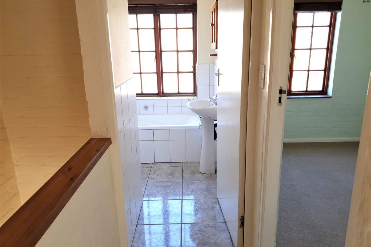 A functional bathroom featuring a pedestal basin and built-in bathtub with tiled finishes, viewed from the adjacent hallway.