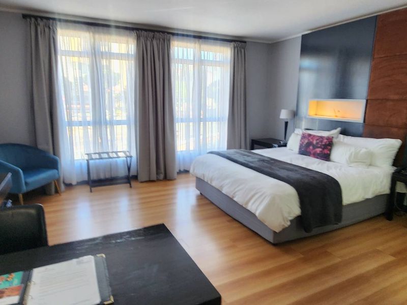 A well-appointed bedroom featuring laminate flooring, a modern built-in headboard with a recessed niche, and large windows with curtains.