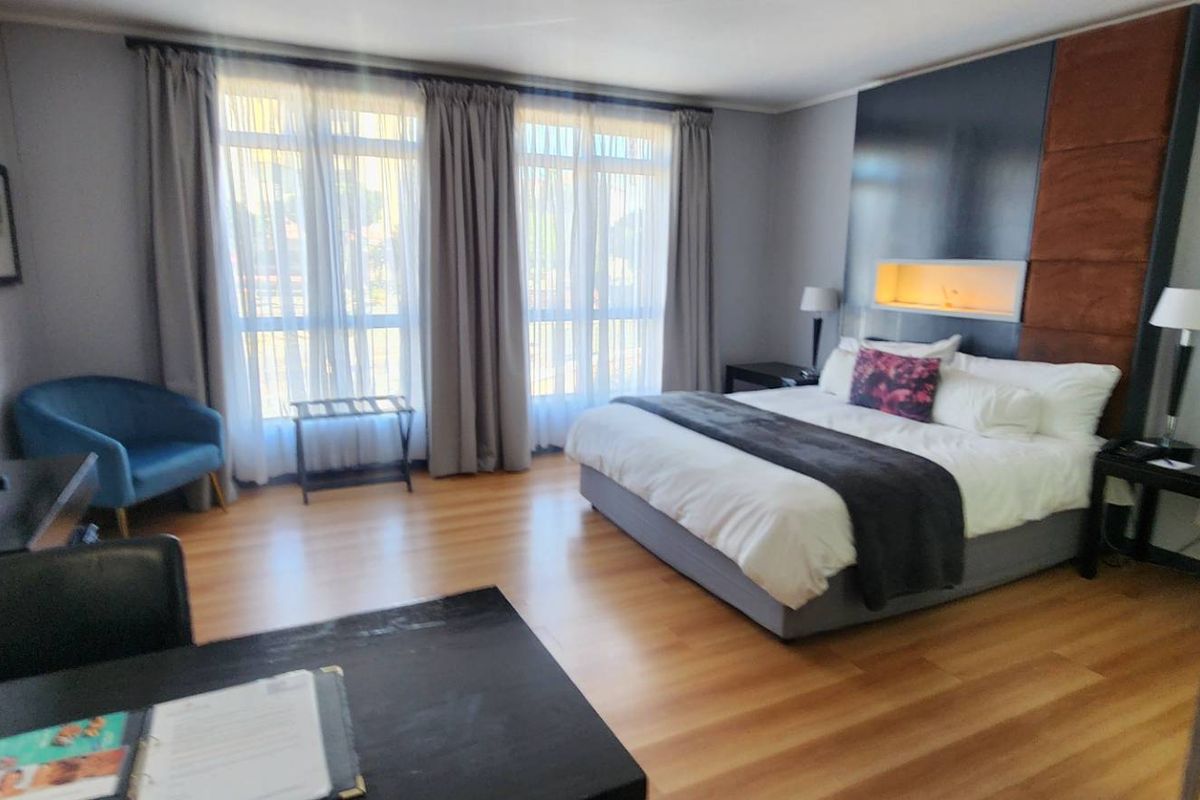 A well-appointed bedroom featuring laminate flooring, a modern built-in headboard with a recessed niche, and large windows with curtains.