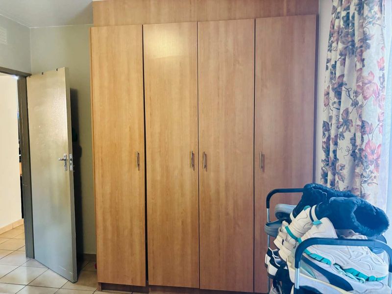 A bedroom featuring a large, wood-finish built-in wardrobe and tiled flooring, providing ample storage space.