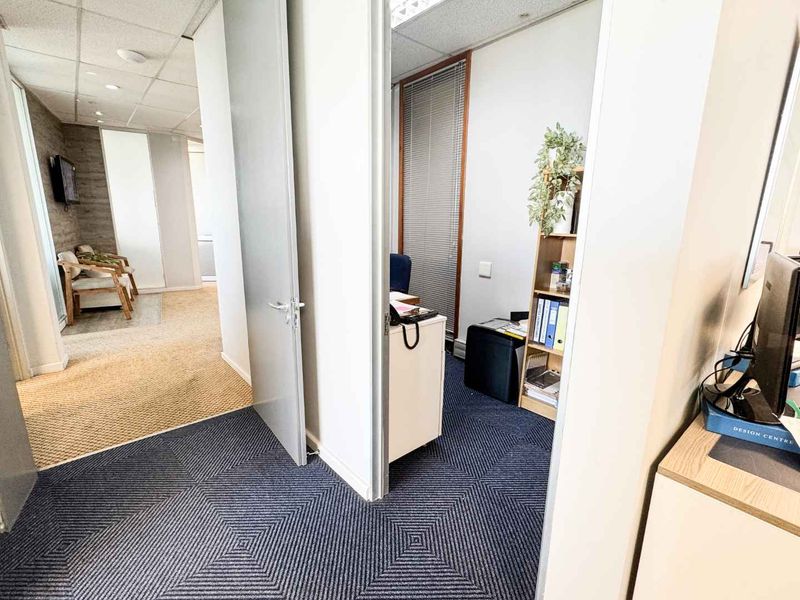 A functional office space featuring a connected layout with carpeted flooring, suspended ceilings, and internal access doors between work areas.