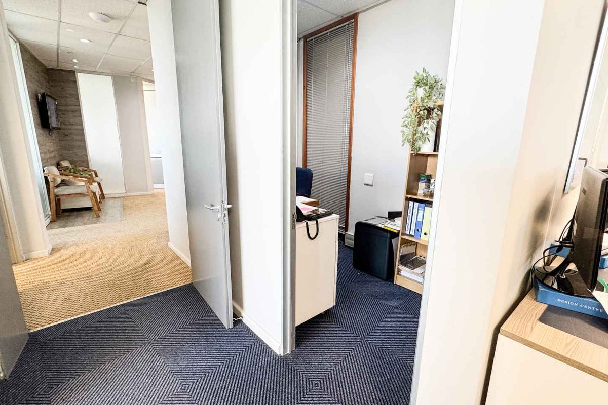 A functional office space featuring a connected layout with carpeted flooring, suspended ceilings, and internal access doors between work areas.