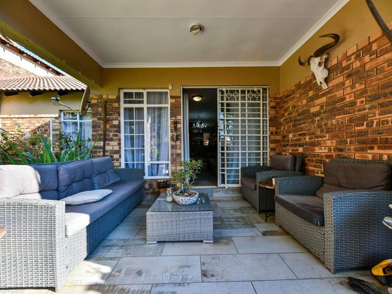 A covered patio area featuring exposed brick walls, tiled flooring, and direct access to the interior through a sliding glass door with security gate.