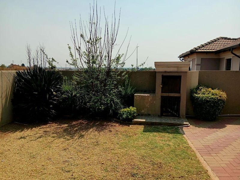 Rear garden area featuring a paved patio, built-in braai structure, and perimeter boundary wall.