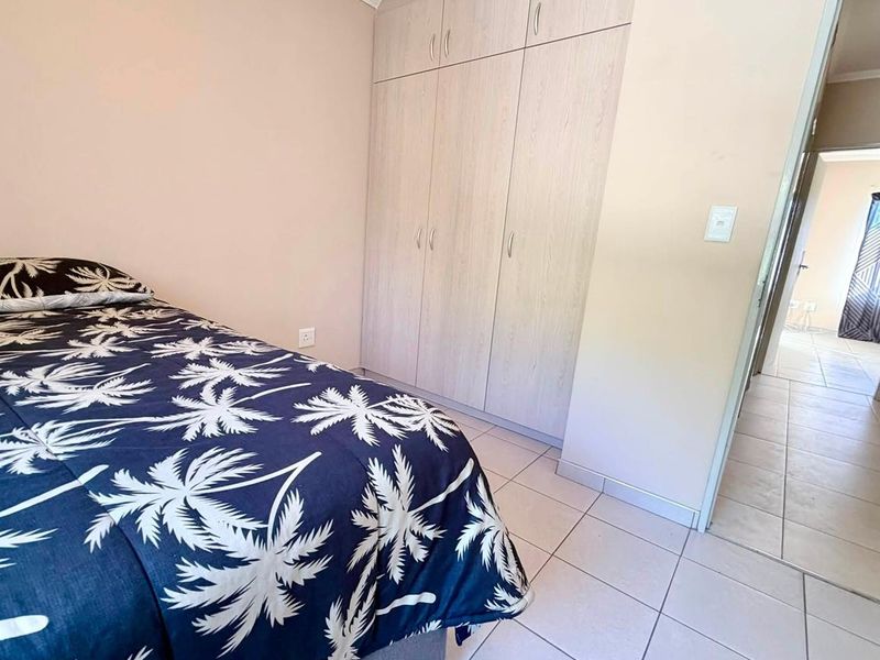 A bedroom featuring built-in cupboards and tiled flooring, with a view leading into the hallway.