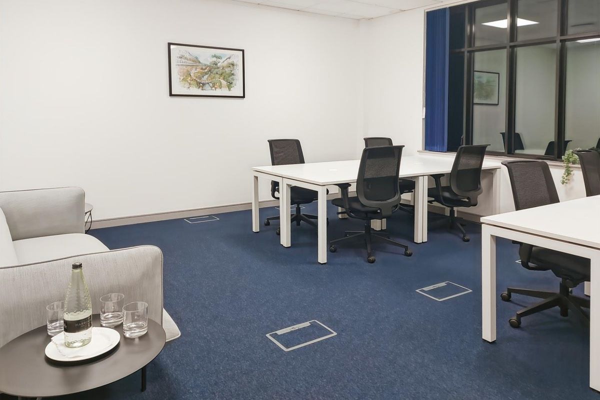 A professional office space featuring blue carpeting, recessed floor power outlets, and a large window with a dark frame.