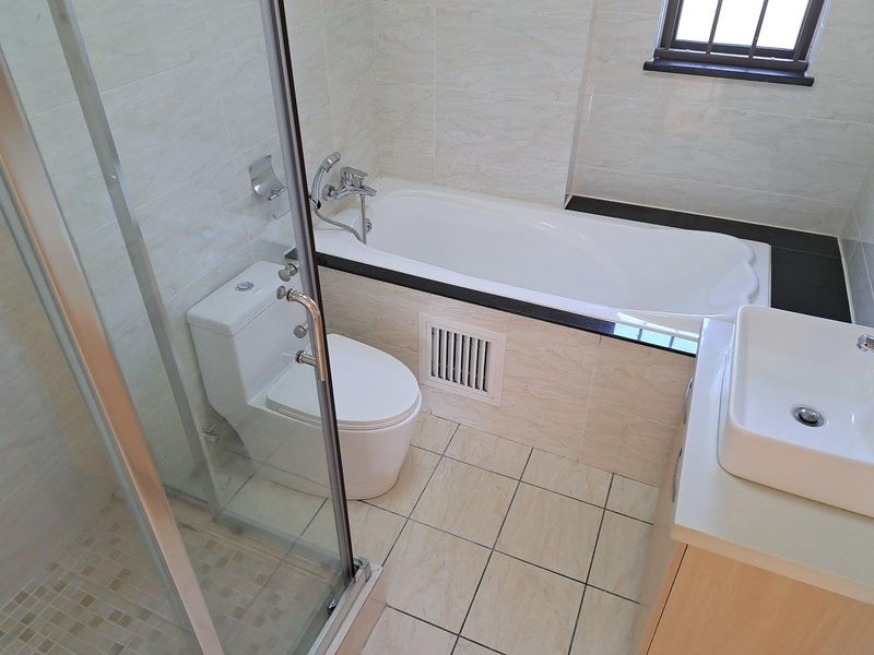 A clean, modern bathroom featuring a separate bathtub, glass-enclosed shower, vessel sink vanity, and neutral wall and floor tiling.