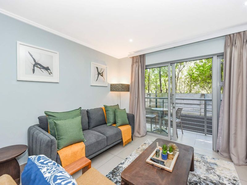 A bright and well-maintained living room featuring tiled floors, recessed lighting, and direct access to a private balcony through sliding glass doors.