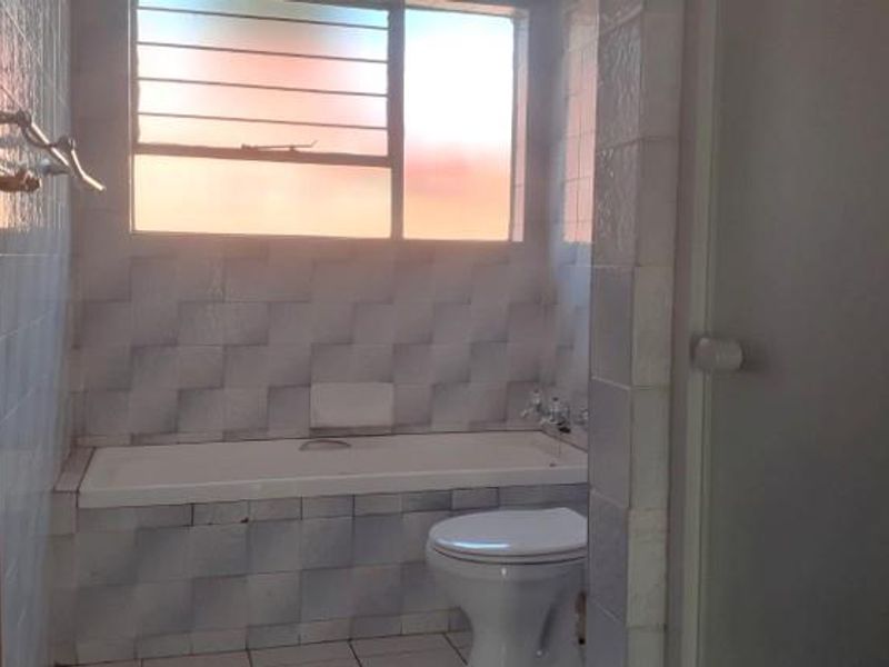 A dated bathroom featuring a built-in bathtub, toilet, and tiled finishes, requiring modernization to improve its aesthetic and functional appeal.