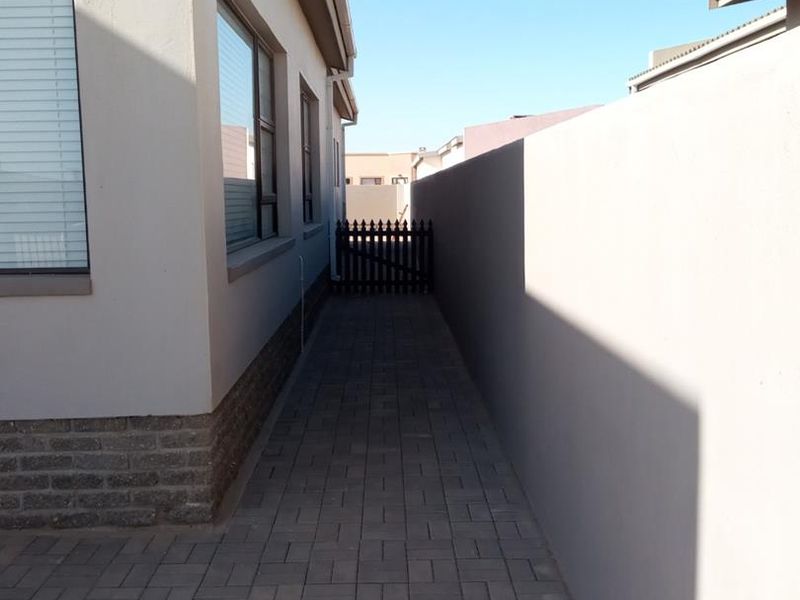 A clean side passage featuring paved flooring, a solid boundary wall, and a secure gate providing access to the rear of the property.