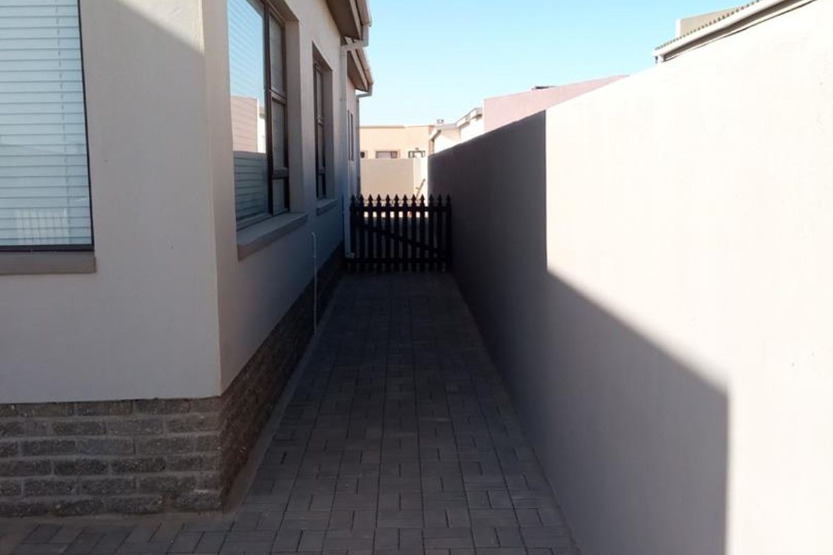 A clean side passage featuring paved flooring, a solid boundary wall, and a secure gate providing access to the rear of the property.