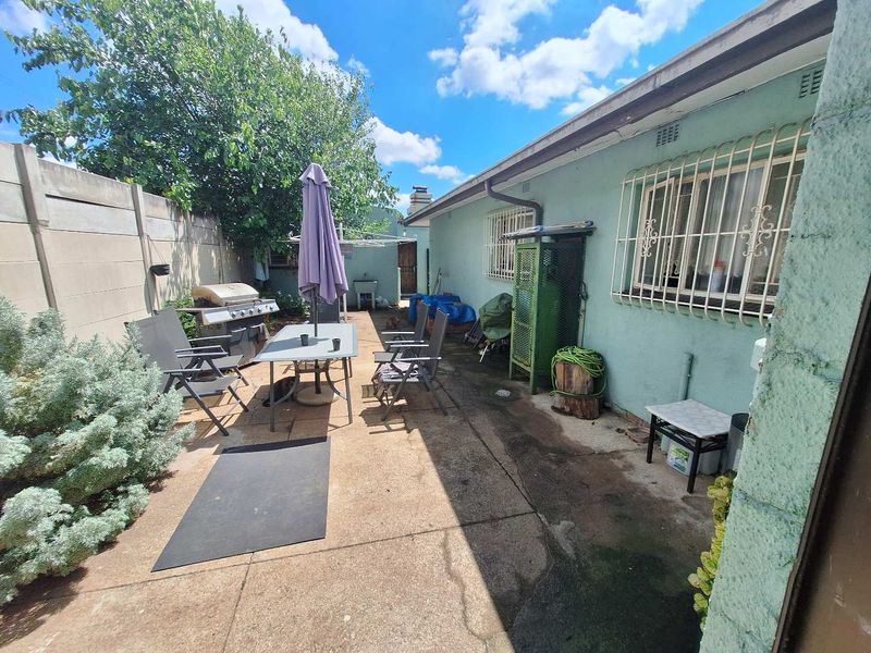 Rear exterior patio area featuring concrete paving, security bars on windows, and a boundary wall, offering potential for outdoor living space improvement.