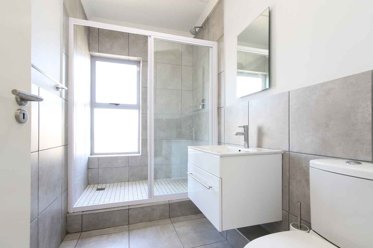 A modern, clean bathroom featuring a walk-in shower with glass enclosure, a wall-mounted vanity unit, and neutral grey tiling throughout.