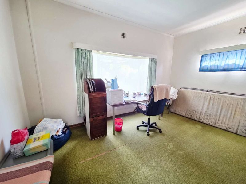 A bedroom featuring large windows and dated green carpeting, offering a blank canvas for potential renovation and modernization.
