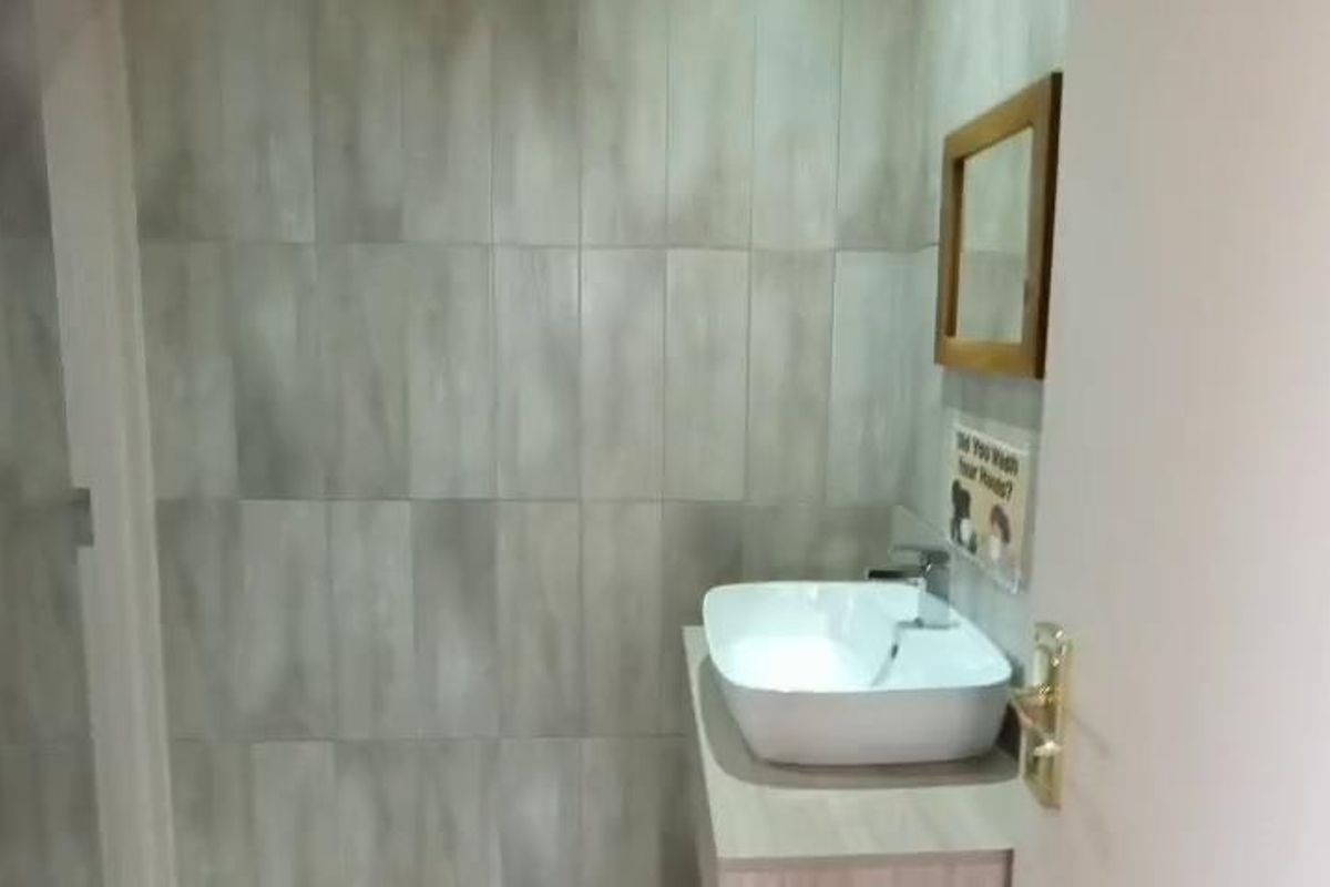 A clean, modern office bathroom featuring a vessel sink, vanity cabinet, and neutral wall tiling.