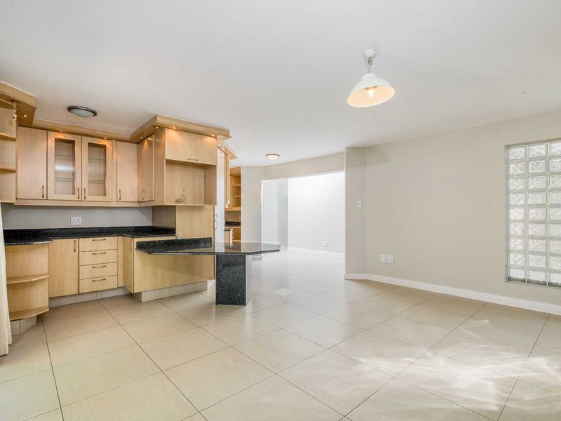 Spacious open-plan kitchen and living area featuring light wood cabinetry, granite countertops, tiled flooring, and a unique glass block feature window.