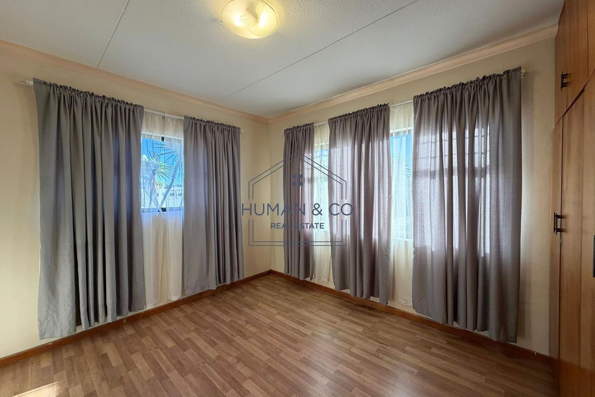 A bright, empty bedroom featuring laminate flooring, built-in cupboards, and large windows with curtain rails.