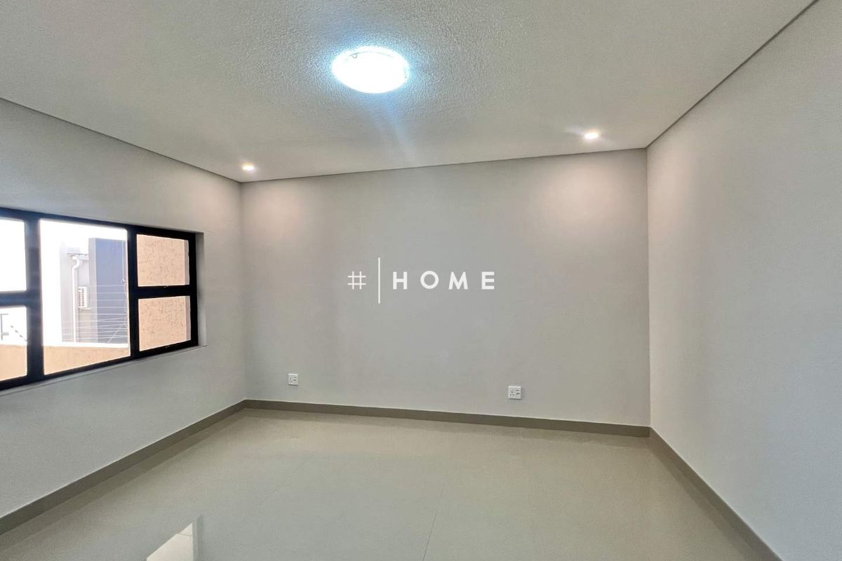 A clean, modern, and empty bedroom featuring neutral tiled flooring, recessed ceiling lighting, and large aluminium-framed windows.