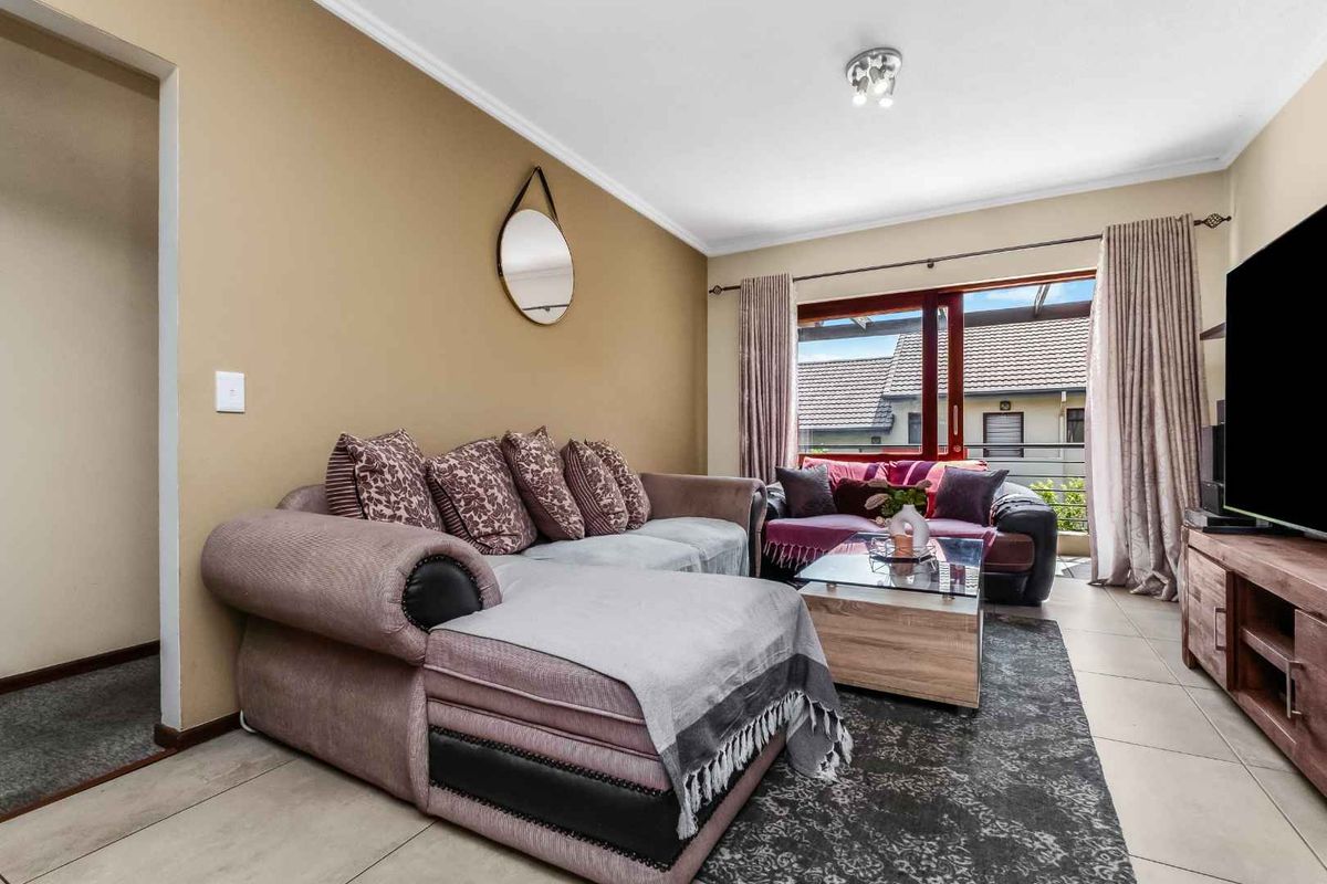A comfortable living room featuring tiled flooring, neutral wall tones, and a sliding glass door providing access to an outdoor balcony area.