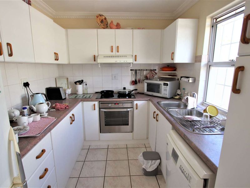 A functional U-shaped kitchen featuring white cabinetry, laminate countertops, built-in oven, electric hob, and a double stainless steel sink with tiled backsplash.