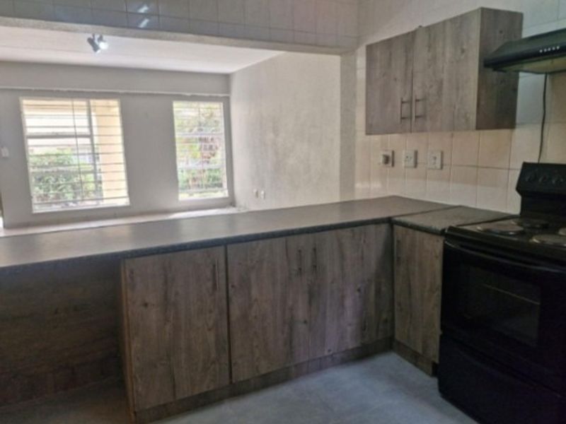 Open plan kitchen area featuring wood-look cabinetry, laminate countertops, and a tiled backsplash, flowing into a bright living space with security-barred windows.