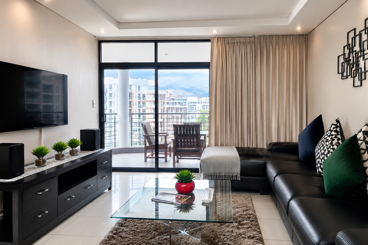 A modern, well-maintained living room featuring tiled floors, recessed ceiling lighting, and a large sliding glass door leading to a private balcony.
