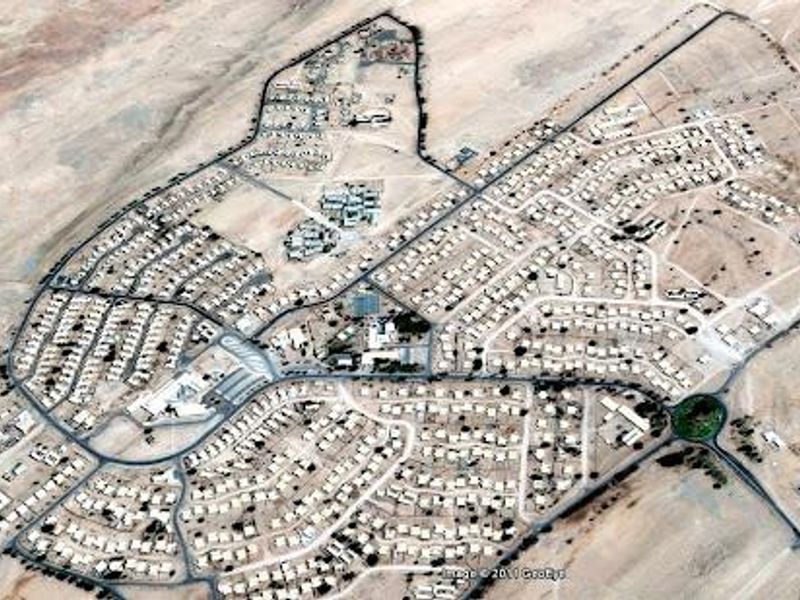 An aerial view of a large residential development featuring a structured road network and multiple housing plots in a desert landscape.
